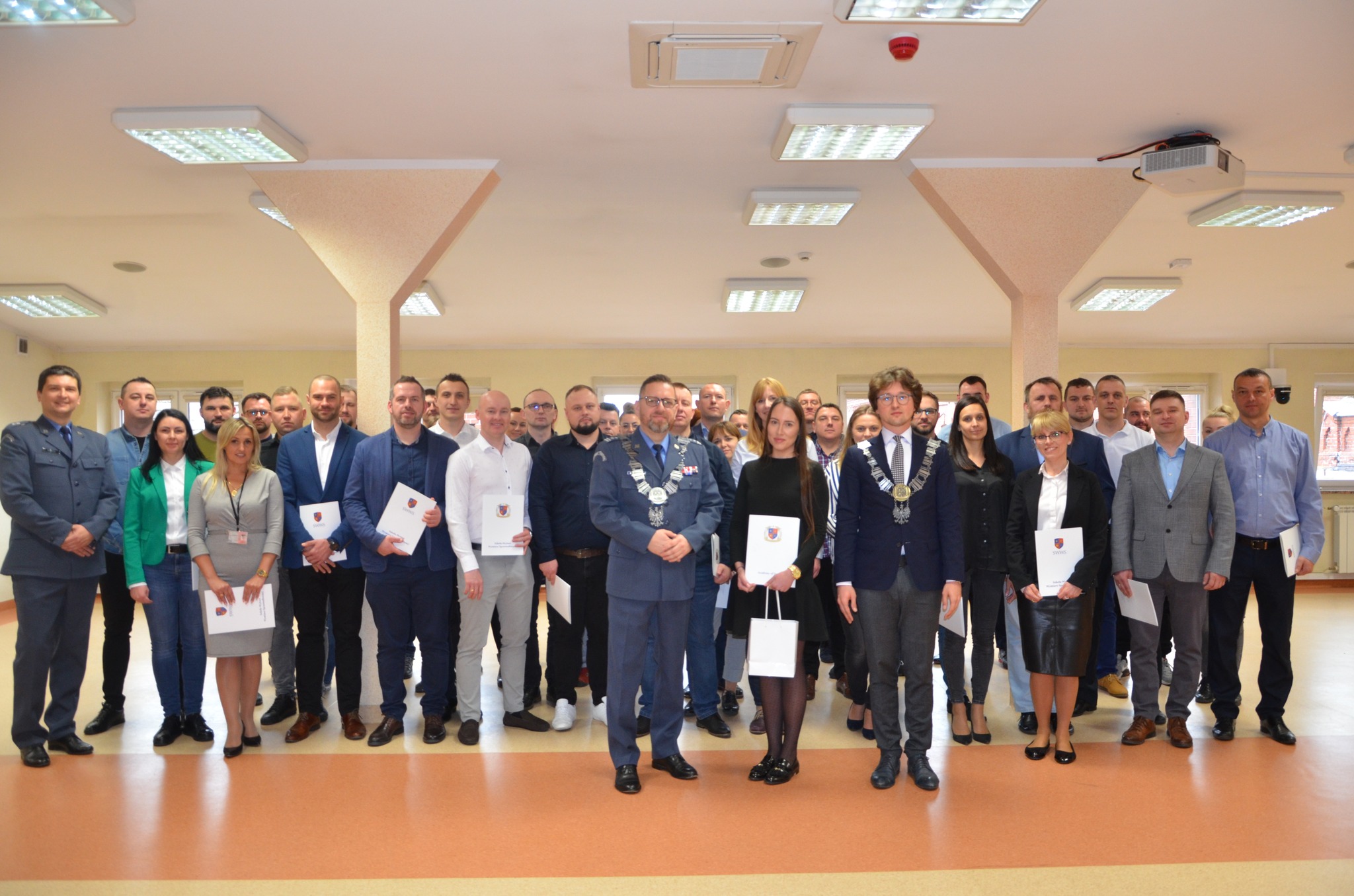 Grupa osób pozuje do wspólnego zdjęcia podczas ceremonii wręczenia dyplomów ukończenia studiów. Na pierwszym planie władze uczelni. 