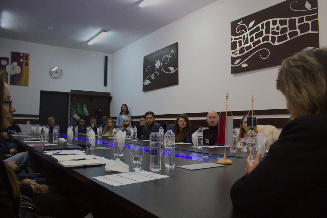 Uczestnicy wizyty studyjnej siedzą przy dużym stole obrad. Na stole flagi Polski i Rumunii oraz notatki i dokumenty.