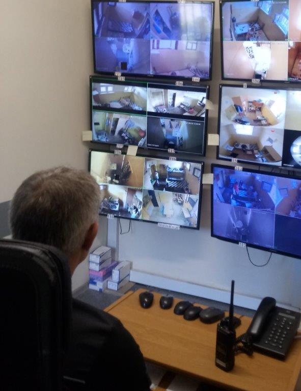 Mężczyzna siedzący na krześle ogląda na kilku monitorach podgląd z cel więźniów.