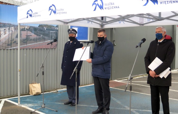 Three men with their face masks at the microphones during the speech. A tent with the Prison Service logo is stretching above them.  