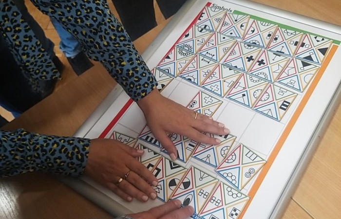 Na stole leży plansza do gry z kolorowymi kartami. Kilka dłoni dotyka planszę i trzyma karty. Na stole leży plansza do gry z kolorowymi kartami. Kilka dłoni dotyka planszę i trzyma karty.