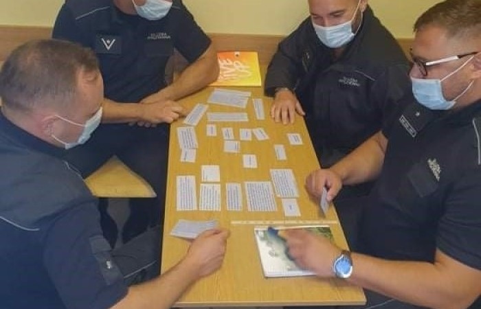 Four men wearing face masks and official outfits are sitting at the table, putting the jigsaw puzzle together. Four men wearing face masks and official outfits are sitting at the table, putting the jigsaw puzzle together.