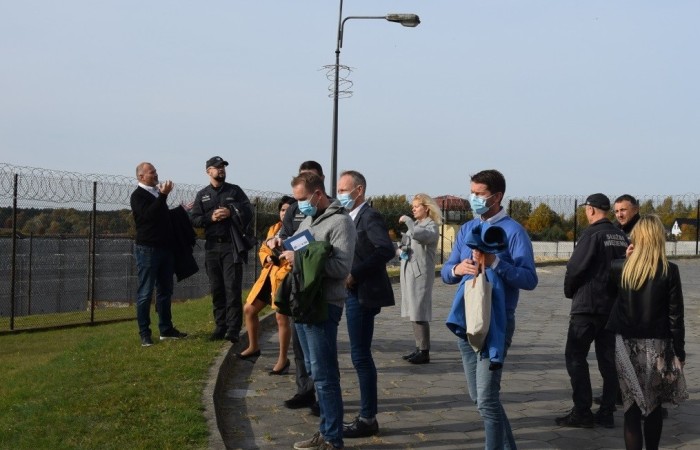 A group of people is talking outside. A couple of persons are wearing Prison Service uniforms. In the background, there is a barbed wire fence. A group of people is talking outside. A couple of persons are wearing Prison Service uniforms. In the background, there is a barbed wire fence.