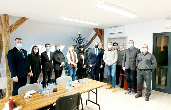 Grupa ludzi w maseczkach pozuje do wspólnego zdjęcia w gabinecie. Przed nimi stół i krzesła, za nimi choinka z bombkami. Grupa ludzi w maseczkach pozuje do wspólnego zdjęcia w gabinecie. Przed nimi stół i krzesła, za nimi choinka z bombkami.