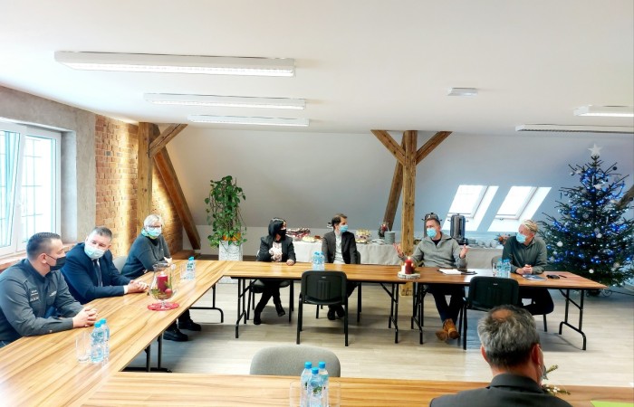 A group of people wearnig face masks is sitting at joined tables, and talking. On the right, there is a decotrated Christmas tree. A group of people wearnig face masks is sitting at joined tables, and talking. On the right, there is a decotrated Christmas tree.