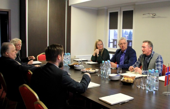 Sześć osób prowadzi dyskusję w gabinecie po dwóch stronach stołu. Na brązowym blacie stołu leżą notatniki oraz woda do picia. Sześć osób prowadzi dyskusję w gabinecie po dwóch stronach stołu. Na brązowym blacie stołu leżą notatniki oraz woda do picia.