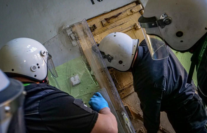 Grupa funkcjonariuszy Służby Więziennej przygotowuje się do otwarcia celi zakładu karnego. Na ich głowach kaski z osłonami twarzy. Grupa funkcjonariuszy Służby Więziennej przygotowuje się do otwarcia celi zakładu karnego. Na ich głowach kaski z osłonami twarzy.