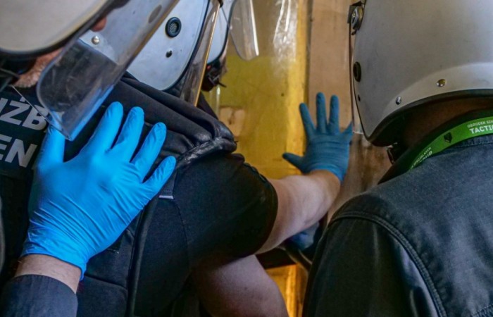 Funkcjonariusze Służby Więziennej otwierają drzwi celi zakładu karnego. Na ich głowach kaski z osłonami twarzy. Funkcjonariusze Służby Więziennej otwierają drzwi celi zakładu karnego. Na ich głowach kaski z osłonami twarzy.