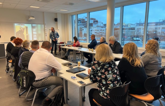 Grupa uczestników wizyty w Norwegii przysłuchuje się prelekcji prowadzącego w sali wykładowej. Po prawej stronie panorama norweskiego miasta za oknami. Grupa uczestników wizyty w Norwegii przysłuchuje się prelekcji prowadzącego w sali wykładowej. Po prawej stronie panorama norweskiego miasta za oknami.