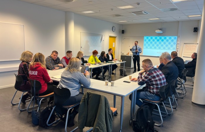 Funkcjonariusz Służby Więziennej z Norwegii prowadzi prelekcję dla uczestników spotkania, siedzących przy stole w kształcie litery Funkcjonariusz Służby Więziennej z Norwegii prowadzi prelekcję dla uczestników spotkania, siedzących przy stole w kształcie litery