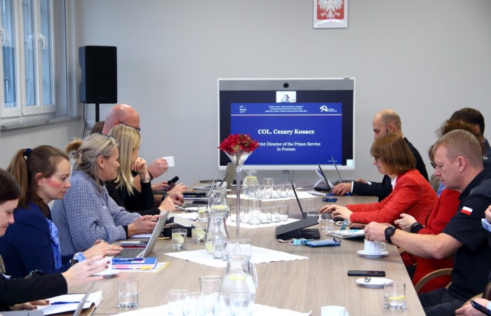 Grupa osób zajmuje miejsca po obu stronach stołu konferencyjnego. W tle szara ściana i ekran urządzenia multimedialnego. Grupa osób zajmuje miejsca po obu stronach stołu konferencyjnego. W tle szara ściana i ekran urządzenia multimedialnego.