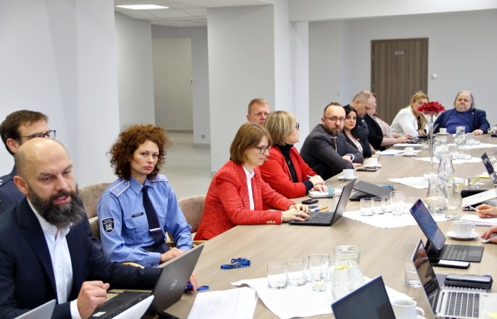 Grupa osób siedzi przy jednej stronie stołu konferencyjnego. Na stole laptopy, notatki służbowe oraz dokumenty. Grupa osób siedzi przy jednej stronie stołu konferencyjnego. Na stole laptopy, notatki służbowe oraz dokumenty.